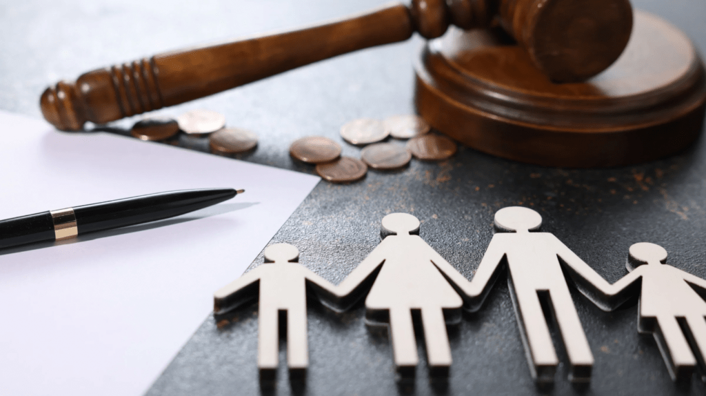 Martelo de juiz de madeira e moedas ao fundo com figuras de papel representando uma família em primeiro plano, simbolizando decisões de pensão e guarda.