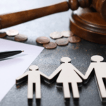 Martelo de juiz de madeira e moedas ao fundo com figuras de papel representando uma família em primeiro plano, simbolizando decisões de pensão e guarda.